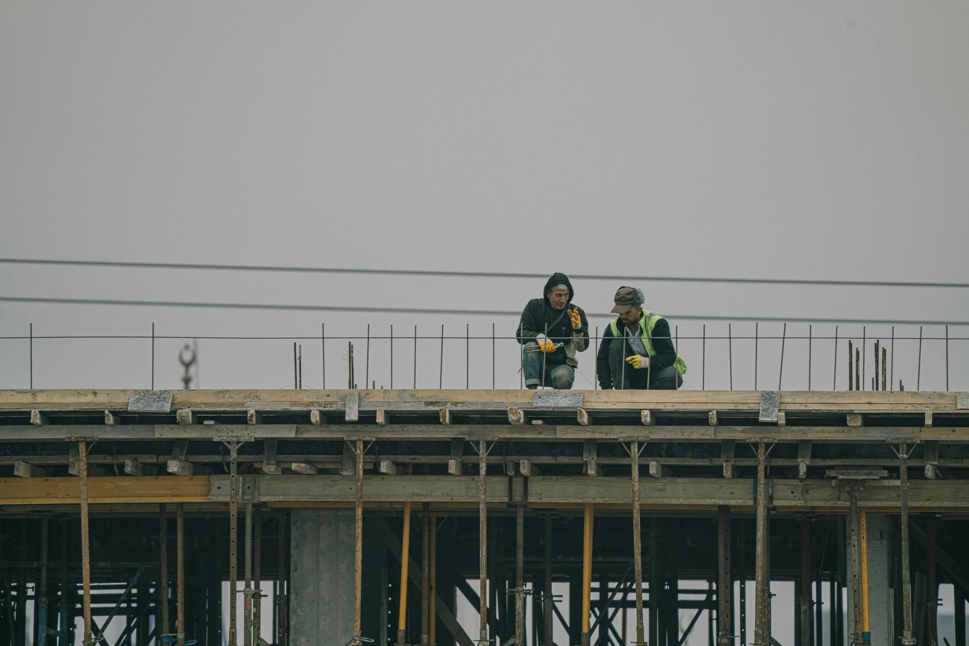 Two construction workers sitting and discussing on top of a scaffolding